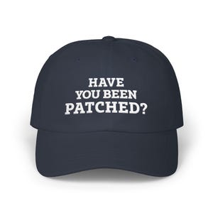 May include: Navy blue baseball cap with the text "HAVE YOU BEEN PATCHED?" in white block letters. The cap has a curved brim and a structured crown. A casual accessory for everyday wear.