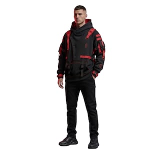 Op de afbeelding: Een zwarte hoodie met rode accenten en bandjes, gecombineerd met een zwarte broek en schoenen. De hoodie heeft een uniek ontwerp met meerdere zakken en een hoge kraag. De outfit is modern en stijlvol, geschikt voor casual wear.