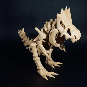 Puede incluir: Figura de esqueleto de dinosaurio beige, que muestra una intrincada estructura ósea. El modelo presenta un cráneo, columna vertebral y extremidades detallados, con garras afiladas y una cresta puntiaguda. El juguete está posado sobre una superficie oscura.