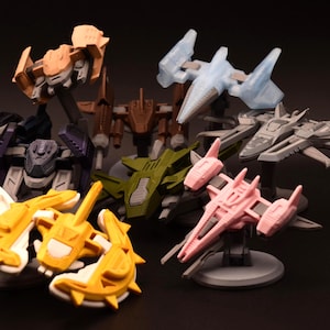 Op de afbeelding: Een verzameling kleurrijke, miniatuur ruimtescheepsmodellen in verschillende ontwerpen en kleuren, waaronder wit, geel, roze, groen en grijs. De modellen worden gepresenteerd op kleine, ronde of rechthoekige bases tegen een donkere achtergrond.