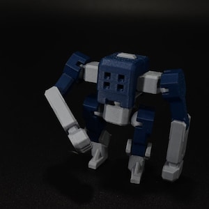 以下が含まれることがあります： 青、グレー、白の色合いの、小さな関節式ロボットのおもちゃ。ロボットは、正方形の頭と4つの正方形の切り欠きがあるブロック状のデザインです。腕と脚はセグメント化されており、機械的な外観になっています。