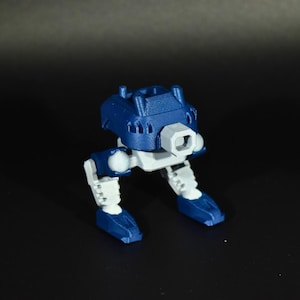 Puede incluir: Un pequeño robot de juguete azul y blanco con una cabeza cuadrada y dos piernas. El robot tiene un cuerpo cuadrado y un elemento gris de forma cuadrada en la parte delantera. Las piernas y los pies son azules y blancos.