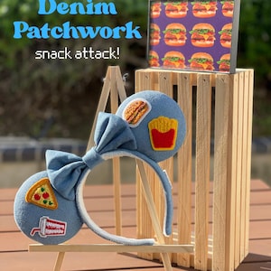 May include: Denim patchwork headband with a large bow and food-themed patches, including pizza, fries, and a burger. The text "Denim Patchwork snack attack!" is visible. A small framed picture of burgers is in the background.