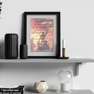 Puede incluir: Una impresión enmarcada con texto persa, exhibida en un estante gris con jarrones negros decorativos y un candelabro. La impresión tiene un marco negro y presenta un fondo colorido. Una campana de cristal y un libro también están en el estante.