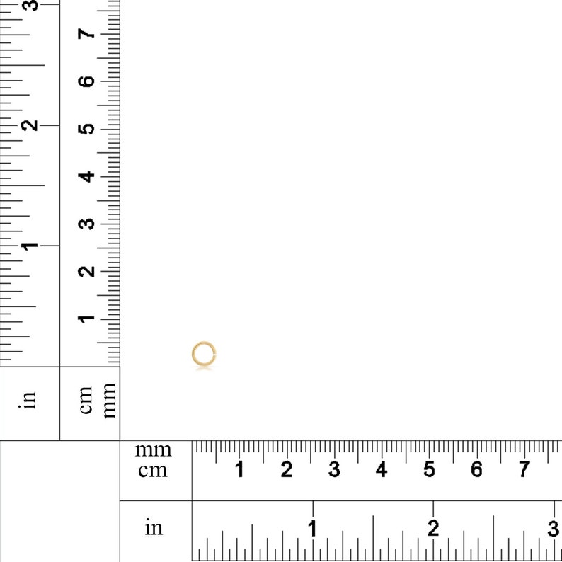K&ouml;nnte beinhalten: Ein kleiner, goldfarbener Sprungring mit einem Durchmesser von etwa 4 mm ist vor einem wei&szlig;en Hintergrund mit einem Lineal als Ma&szlig;stab zu sehen.