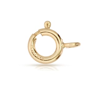 Puede incluir: Cierre de metal dorado con un anillo redondo y un pequeño gancho. El cierre está diseñado para sujetar joyas u otros artículos.