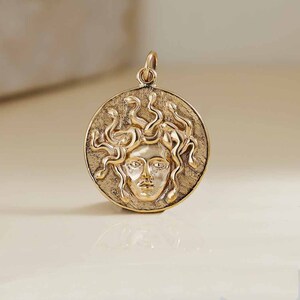 Peut inclure: Pendentif doré en relief représentant le visage de Méduse avec des serpents pour cheveux.