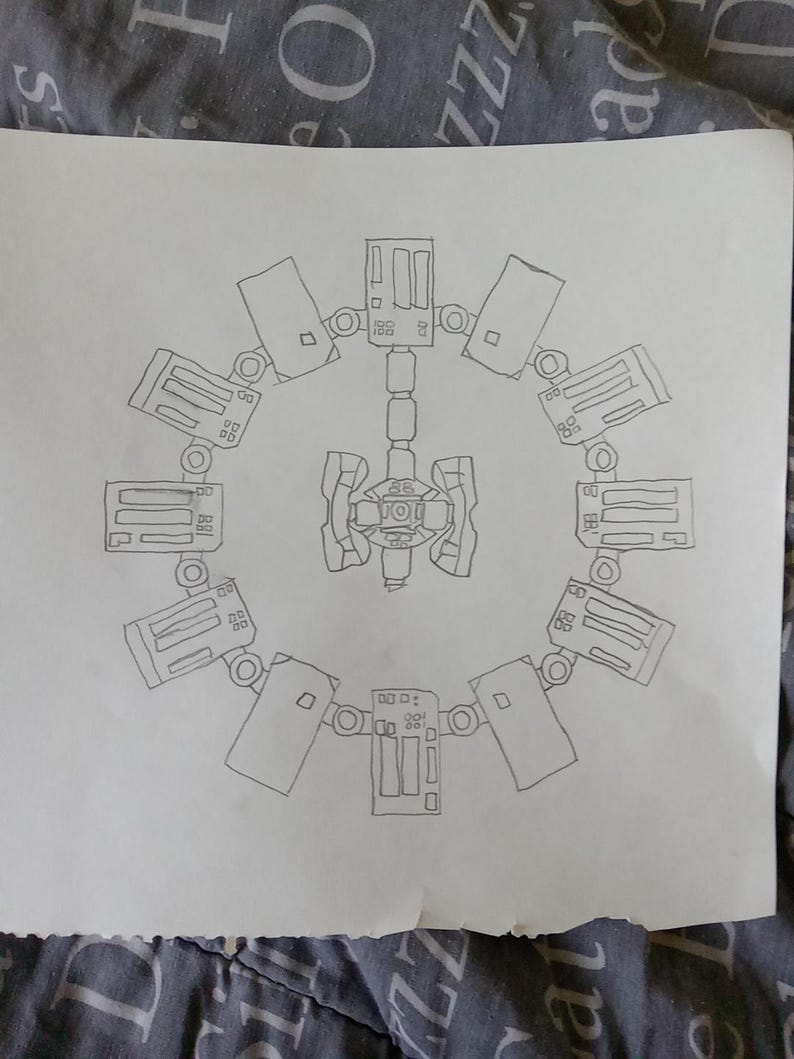 May include: A hand-drawn sketch of a circular space station design. The central hub connects to a ring of rectangular modules, each with detailed panels and circular attachments. The drawing is on a white sheet of paper.