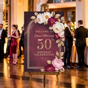 Puede incluir: Un letrero de bienvenida burdeos sobre un caballete dorado, que anuncia una celebración de 50 cumpleaños. El letrero presenta detalles florales en blanco, rosa y burdeos, con letras doradas. El evento es en Nueva York.