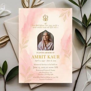 May include: A memorial card featuring a portrait of a woman, gold leaf designs, and text. The text includes "In Loving Memory of Amrit Kaur" and service details. The background has a soft pink watercolour wash.