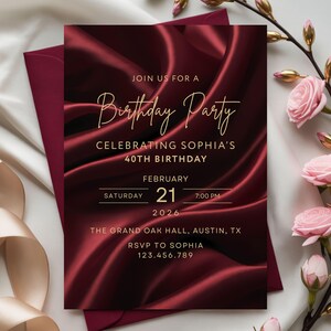 Burgundy silk birthday invitation with gold text styled with envelope and soft floral accents