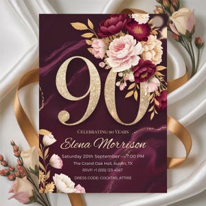Op de afbeelding: Een bordeauxrode uitnodigingskaart met gouden details, met het gouden getal 90, bloemstukken en evenementdetails. De tekst luidt "Celebrating 90 Years" en bevat de naam "Elena Morrison" en evenementinformatie.