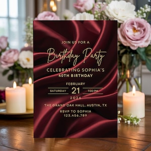 Elegant burgundy silk birthday invitation with gold text styled on table with candles and flowers