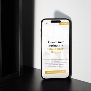 Pu&ograve; includere: Uno smartphone nero mostra un sito web con il testo "Elevate Your Business to Extraordinary Heights". Il telefono &egrave; posizionato su una superficie scura accanto a una struttura nera, con un muro bianco sullo sfondo. Il sito offre servizi di coaching.