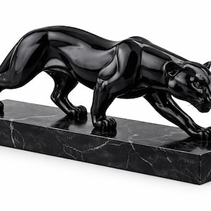 May include: A sleek, black panther sculpture with green eyes, in a stalking pose. The big cat is mounted on a rectangular black marble base. This decorative piece is suitable for home decor. The base is approximately 30 cm long.