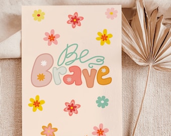 May include: A rectangular card with the words "Be Brave" in colorful, bubble-style letters. The card is decorated with various colorful flowers. The background is a light peach color.