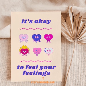 May include: A cream-colored card with the text "It's okay to feel your feelings" in purple. The card features six cartoon hearts in various colors and expressions, including pink, blue, and red. The card has a whimsical and encouraging design.