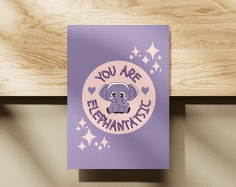May include: A lavender card with a circular design featuring a cartoon elephant and the words "You Are Elephantastic." The design includes hearts and starbursts. The card is on a wooden surface.