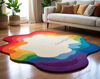 May include: A colorful, abstract rug with a rainbow design. The rug features a white center surrounded by layers of red, orange, yellow, green, blue, and purple. The rug is placed on a hardwood floor in a living room setting.