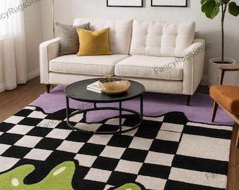 May include: A modern living room rug with a unique design. The rug features a black and white checkerboard pattern that transitions into a green, blob-like shape. A white sofa, black coffee table, and framed art complete the room.