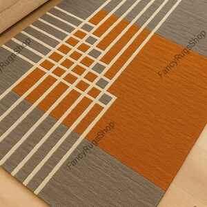 Könnte beinhalten: Rechteckiger Teppich mit geometrischem Muster in Grau, Orange und Creme. Der Teppich hat ein modernes Design mit sich kreuzenden Linien und Farbblöcken. Der Teppich scheint aus gewebtem Material zu sein.
