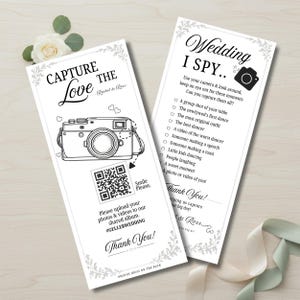 May include: Two white wedding cards with black text and illustrations. One card says "Capture the Love" with a camera graphic and a QR code. The other says "Wedding I Spy" with a list of photo prompts.