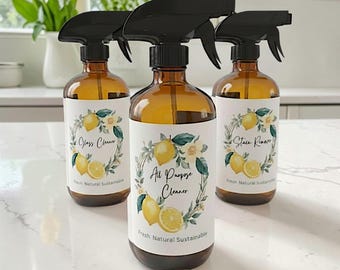 May include: Three amber glass spray bottles with black triggers. Each bottle features a white label with a lemon and leaf wreath illustration. The labels are printed with the text Glass Cleaner, All Purpose Cleaner, and Stain Remover.