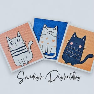 May include: Three Swedish dishcloths with cat illustrations. One cloth has a white cat with black stripes, another has a white cat with glasses and hearts, and the third has a black cat with a curly tail. The text "Swedish Dishcloths" is below the cloths.