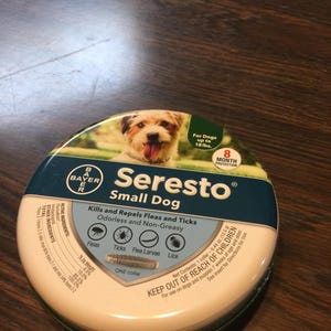 May include: A round container of Seresto flea and tick collar for small dogs. The label features a dog image, the Bayer logo, and text indicating 8-month protection. It kills and repels fleas, ticks, flea larvae, and lice.