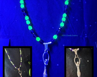 May include: A necklace featuring alternating dark blue and neon green glow-in-the-dark beads with a silver-toned metal pendant shaped like a stylised female figure. The text 2026 (c) Deadly Creations is visible near the pendant in the main image.