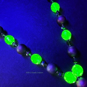 May include: A necklace featuring alternating matte dark purple spherical beads and faceted bright neon green beads that glow under ultraviolet light. The necklace includes small dark spacer beads and the text 2026 (c) Deadly Creations.