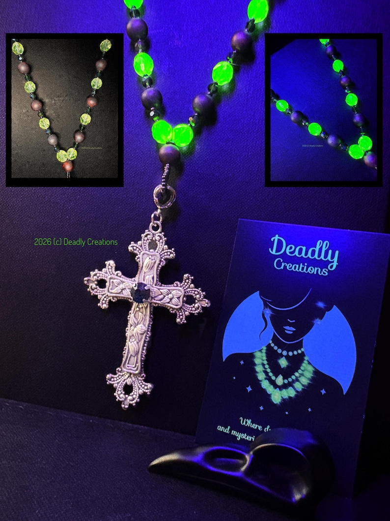 May include: A necklace featuring a silver-toned ornate cross pendant with a central dark stone, suspended from a strand of alternating matte dark beads and vibrant neon green glow-in-the-dark beads. A black display card with the text Deadly Creations.