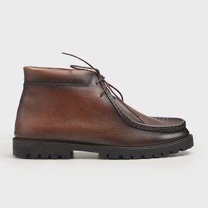 May include: Brown leather ankle boot with a lug sole. The boot features a moccasin-style toe and lace-up closure. The leather has a distressed appearance, with darker shading around the edges.