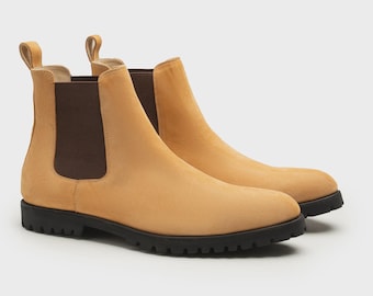 May include: A pair of tan Chelsea boots with a pull tab at the back. The boots have a suede-like texture and a black rubber sole. The elastic side panels are brown. The boots are displayed on a white background.