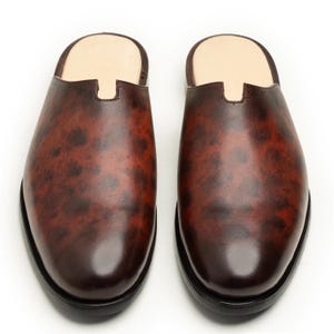 May include: A pair of brown leather slip-on shoes with a mottled pattern. The shoes have a rounded toe and a black sole. The interior is a light tan color.
