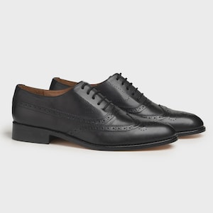 May include: A pair of black leather Oxford shoes with brogue detailing. The shoes have a classic design with a low heel and lace-up closure. The leather has a polished finish, and the shoes are set against a neutral background.