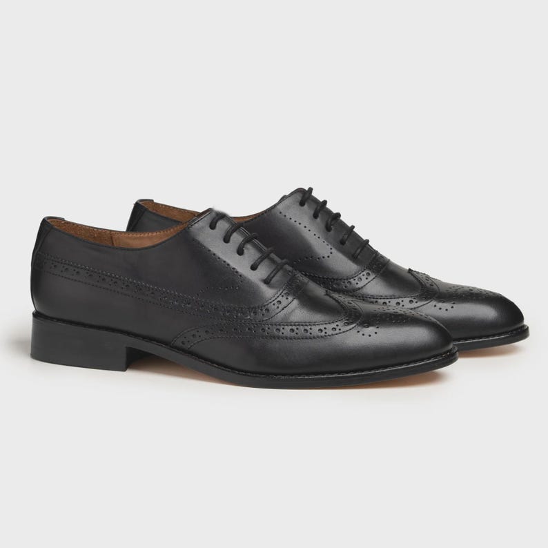 May include: A pair of black leather Oxford shoes with brogue detailing. The shoes have a classic design with a low heel and lace-up closure. The leather has a polished finish, and the shoes are set against a neutral background.