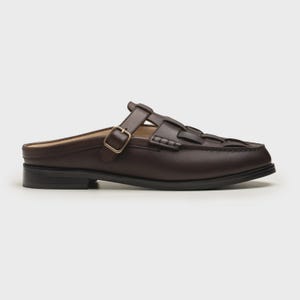 May include: A brown leather mule with a woven vamp design. The shoe features a strap with a gold-colored buckle and a low, black heel. The open-back design offers a slip-on style, suitable for casual or semi-formal wear.