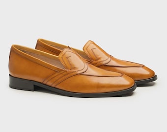 May include: A pair of tan leather loafers with a classic design. The shoes have a smooth, polished finish, a stitched vamp, and a black sole. The loafers are displayed on a neutral background.