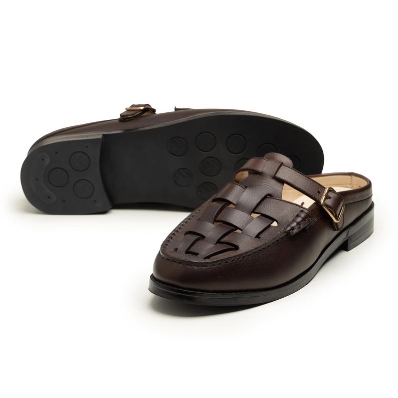 May include: Brown leather slip-on shoes with a woven vamp design and a buckle closure. The shoes have a dark brown sole with a tread pattern. One shoe is upside down, revealing the sole.