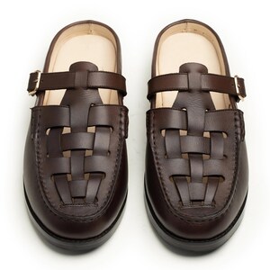 May include: A pair of brown leather clogs with a woven design on the toe and a strap with a buckle. The clogs have a dark sole and a light-colored insole.