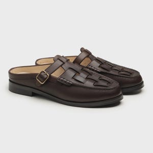 May include: A pair of dark brown leather slip-on shoes with a woven design on the top. The shoes have a small heel and a gold-colored buckle on the side. The shoes are designed for comfort and style.