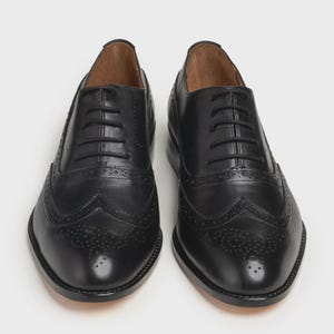 May include: A pair of black leather Oxford shoes with decorative perforations and a lace-up closure. The shoes have a classic wingtip design and a polished finish, suitable for formal occasions.