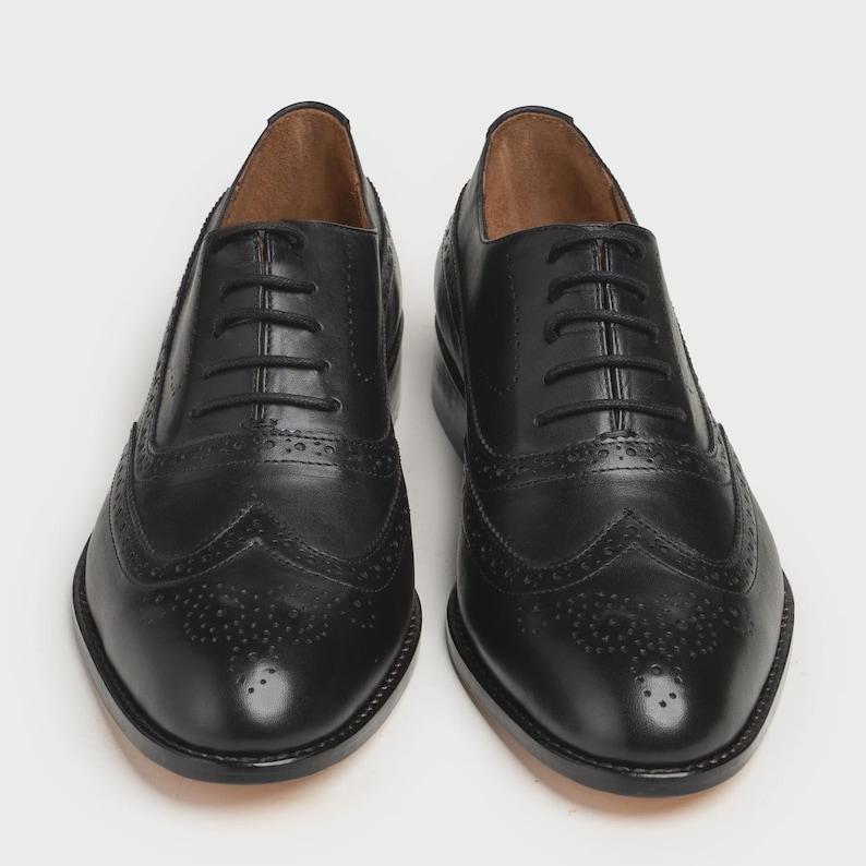 May include: A pair of black leather Oxford shoes with decorative perforations and a lace-up closure. The shoes have a classic wingtip design and a polished finish, suitable for formal occasions.