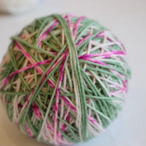 Puede incluir: Una bola de hilo con rayas verdes, blancas y rosas.