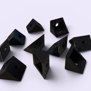 Puede incluir: Un conjunto de diez soportes de esquina triangulares de color negro hechos de material texturizado. Cada soporte presenta dos lados planos que se unen en ángulo recto, con un orificio circular centrado en cada una de las dos caras para montaje.