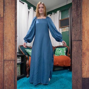 May include: A long, teal-colored dress with long, puffy sleeves and a square neckline. The dress has a slit on the side and is made of a shiny fabric. The dress is a maxi length and is suitable for formal occasions.
