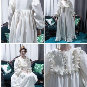 May include: A floor-length cream-colored dress featuring long puffed sleeves, a button-down front placket, and vertical pleats on the bodice. The garment is accented with ruffled trim along the chest and hemline, creating a full, flowing silhouette.