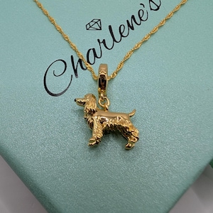 May include: A gold-toned necklace featuring a pendant shaped like a spaniel dog. The pendant hangs from a delicate twisted chain. The jewellery is displayed against a light blue box with the text Charlene's and a small diamond icon printed on it.