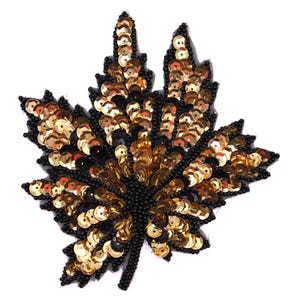 May include: A leaf-shaped applique with a black mesh base. The applique is decorated with gold and black sequins, arranged to resemble the veins and shape of a leaf. The stem is made of black beads.
